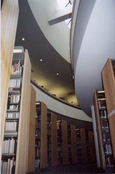 Photo from the lower floor glancing up at the upper floor and skylight while also having a view of the bookshelves at the bottom.